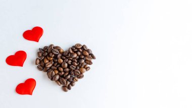 Kahve için aşkın sembolü. Kalp şeklinde kahve çekirdekleri ve beyaz arka planda kırmızı kalpler, kapatın.