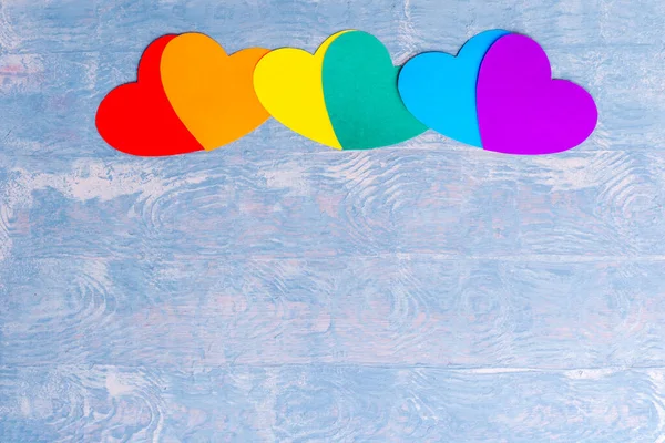 Бумажные сердца ручной работы в ЛГБТ-цветах выстроились в ряд на синем деревянном фоне, плоский узор, пространство для копирования — стоковое фото