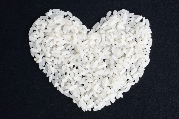 Koncepcja dietetycznego jedzenia. Miłość do ryżu. Niegotowany ryż w kształcie serca na czarnym tle, zbliżenie, widok z góry — Zdjęcie stockowe