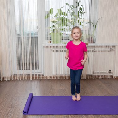 Beyaz tenli sevimli küçük kız evdeki paspasın üzerinde spor yapıyor. Çocuk fitness konsepti