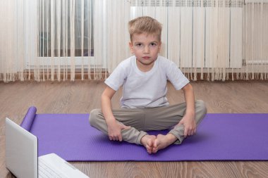 Çevrimiçi fitness konsepti. Beyaz tenli sevimli küçük çocuk evdeki paspasın üzerinde spor yapıyor internetteki kişisel antrenörüyle ders çalışıyor. Çocuk fitness konsepti