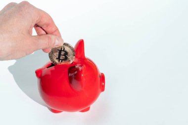 El, beyaz arka planda kırmızı bir kumbara içine bir bitcoin koyar, kopyalama alanı. Yeni mali sistem