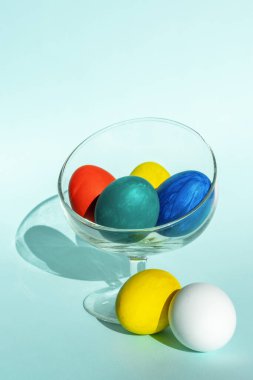 Açık mavi zemin üzerinde şeffaf cam bir kâse içinde el boyaması Paskalya yumurtaları, dikey çerçeve, kopyalama alanı
