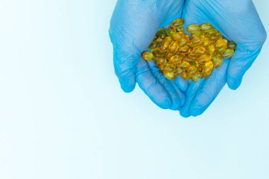 Mavi eldivenli doktorlar sarı omega-3 kapsülleri, vitaminleri ve mavi hapları tutuyor.