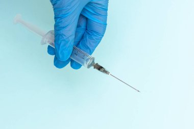 Mavi eldivenli, mavi arka planda ilaç bulunan bir şırıngayı tutan doktorların yakın çekimi.