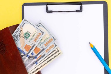 Kahverengi bir cüzdanda dolar ve alışverişler için çarşaf veya yapılacaklar listesi ve sarı bir kaleme mavi bir kalem.