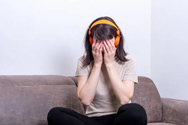 An upset woman listening to music and covering her face with her hands, woman upset after online communication