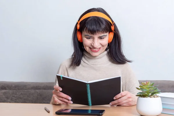 Enseñanza a distancia. Una profesora con un suéter beige y auriculares naranjas está leyendo un libro — Foto de Stock