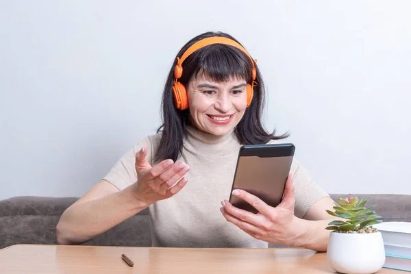 Feliz sonrisa alegre hermosa mujer en auriculares naranjas hablando en línea con amigos en la tableta — Foto de Stock