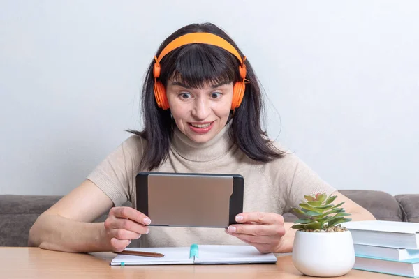 Emocional mujer morena blanca blogger en auriculares naranjas hablando en línea con los suscriptores en la tableta — Foto de Stock