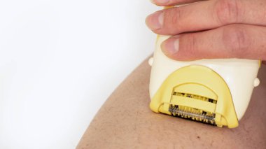 Kadın elinin yakın çekimi bacaklardaki fazla kılları elektrikli jiletle alıyor. Ev güzelliği tedavileri