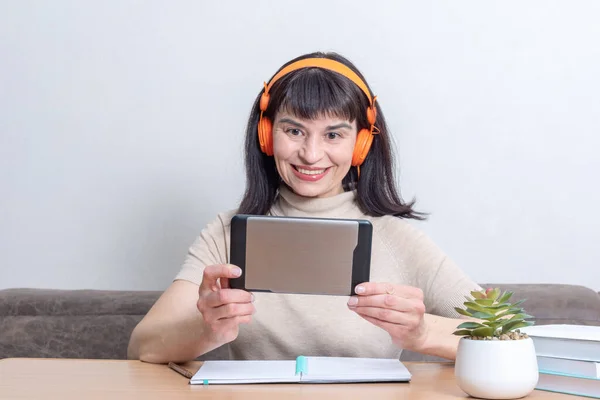 Feliz sonrisa alegre hermosa mujer caucásica en auriculares naranjas hablando en línea con amigos en la tableta — Foto de Stock