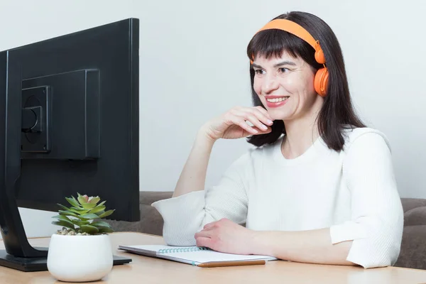Mujer sonriente con auriculares sentada en la mesa mirando la pantalla del monitor, viendo webinar o curso de entrenamiento — Foto de Stock