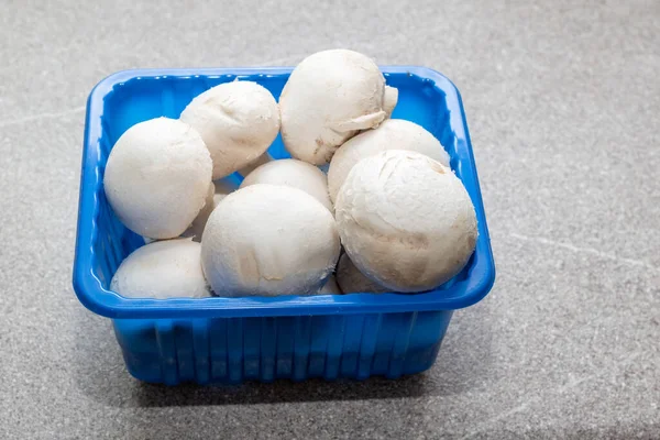 Champignons champignon dans une boîte bleue sur une table de cuisine grise, gros plan. Champignons blancs entiers dans une boîte en plastique. Aliments naturels sains. Concept alimentaire diététique — Photo