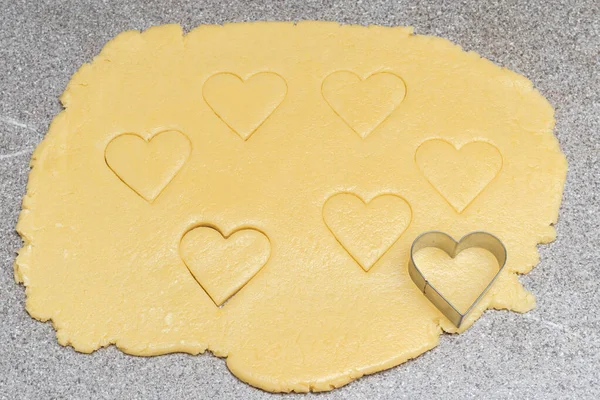 Biscotti tagliati a cuore e forma di cuore per tagliare su pasta cruda gialla su uno sfondo grigio tavolo — Foto Stock