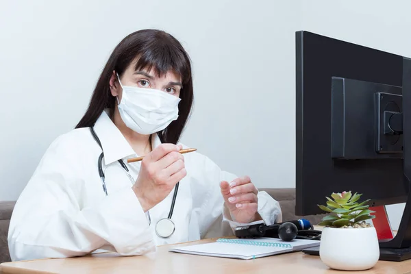 Una doctora con una máscara protectora médica te está mirando mientras estás sentada en una mesa en el consultorio.. — Foto de Stock