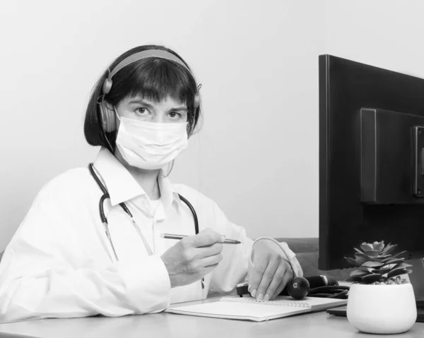 Una doctora con una máscara protectora médica te mira mientras estás sentada en una mesa en un consultorio, en blanco y negro. El médico escucha a los pacientes síntomas, diagnóstico. — Foto de Stock