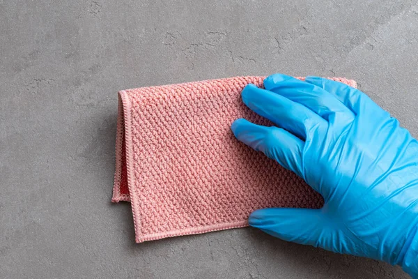 Уборка дома. Рука в голубой латексной перчатке трёт розовую тряпку из микроволокна по серой штукатурке крупным планом. — стоковое фото