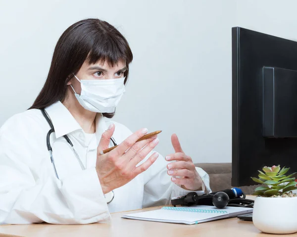 Una mujer médico con una máscara médica hace una videollamada en línea, discute, gestos. Videoconferencia de telemedicina — Foto de Stock