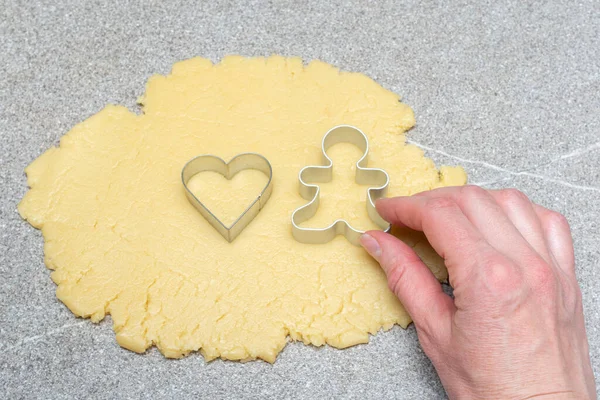 Una mano tiene un tagliabiscotti a forma di cuore e pan di zenzero su pasta arrotolata per cuocere biscotti fatti in casa — Foto Stock