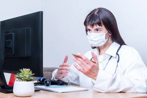 Una mujer médico con una máscara médica hace una videollamada en línea, discute, gestos. Reunión virtual de aplicaciones informáticas remotas de videoconferencia de telemedicina — Foto de Stock
