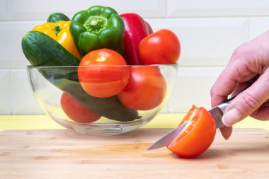Bıçak tutan bir el domates ve çok renkli taze biber, domates ve salatalığı kasede keser.