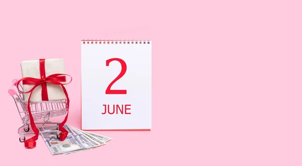 En presentask i en kundvagn, dollar och en kalender med datum 2 juni på en rosa bakgrund. — Stockfoto