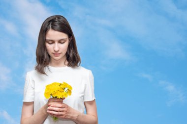 Güzel beyaz kız elinde bir buket sarı karahindiba tutuyor bulutlu mavi gökyüzüne, kopyala uzay