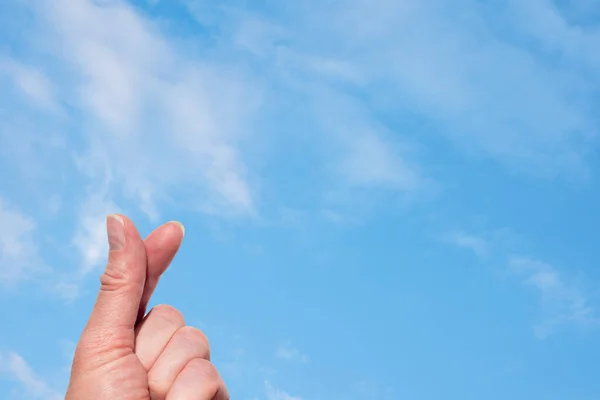 A hand making a heart shape with two fingers against the background of a blue sky with white fluffy clouds. — Stockfoto