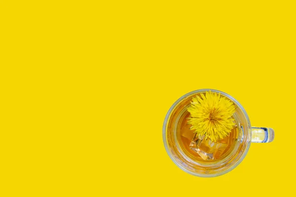 Healthy herbal tea with dandelions in a glass cup, ice and yellow dandelion flower inside on a yellow background, top view, copy space, close-up. Healthy eating concept — Photo