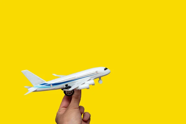 Hand holding toy white airplane on bright yellow background, copy space. Travel, vacation, vacation concept