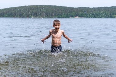 Sevimli mutlu çocuk göle su sıçratıyor. Çocuk güneşli bir günde gölde banyo yapar. Neşeli mutlu çocukluk konsepti