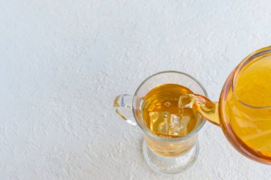 Şeffaf bir fincana, beyaz arka planda şeffaf bir çaydanlıktan bitki çayı dökmek, boşluğu kopyalamak.