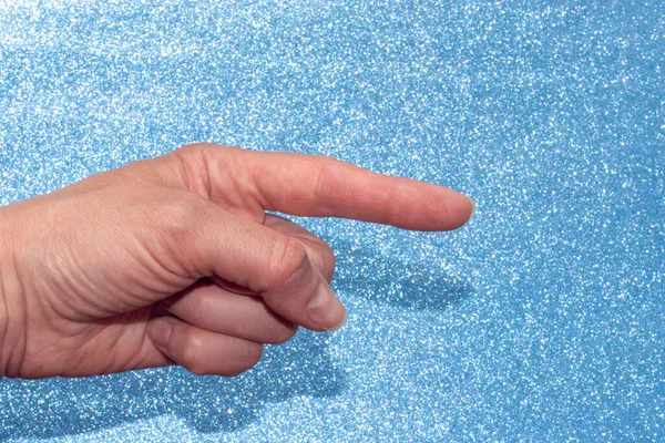 Weibliche Hand, die mit dem Finger auf einen blau glitzernden Hintergrund zeigt. Layout für Ihre Anzeige — Stockfoto