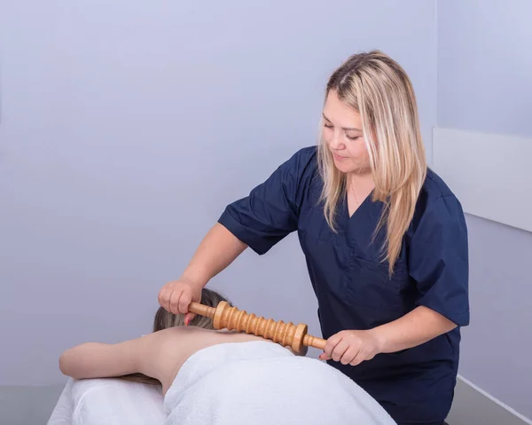 Mujer bonita masajista masajea a los pacientes con un masajeador de rodillos de madera. Mujer teniendo masaje de spa en el salón de belleza. Tratamiento del dolor de espalda con masaje, terapia con Madero. —  Fotos de Stock