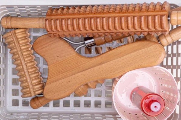 Madero terapia, masaje relajante anti-celulitis - instrumentos de masaje de madera con punta de rodillo, rodillo, placa, aceite de masaje en una cesta de color rosa, vista superior, primer plano — Foto de Stock