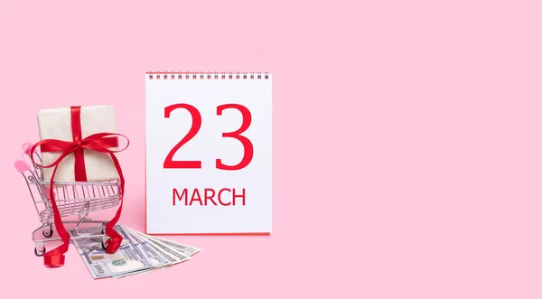 쇼핑 트롤리에 있는 선물 상자, 달러, 핑크 색 배경에 23 행진 날짜와 달력. — 스톡 사진