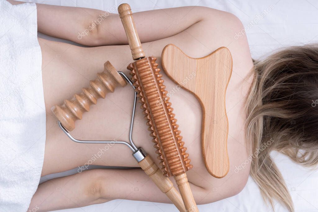 Madero therapy, anti-cellulite relaxing massage - wooden massage tools roller spiked, rolling pin, plate lying on a womans back, top view, close-up