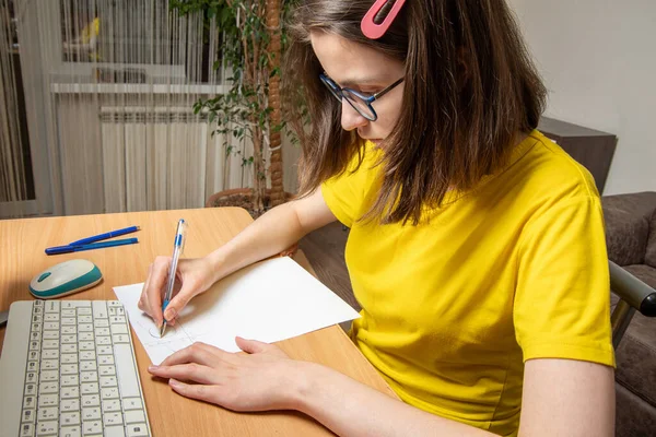 Retrato de una hermosa chica caucásica en una camiseta amarilla, escribe un esquema, trabajo en casa, aprendizaje a distancia — Foto de Stock