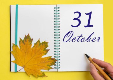 Ekim 'in 31' inde. 31 Ekim tarihini açık bir deftere el yazısıyla yazmak. Sarı arka planda güzel bir doğal akçaağaç yaprağı. Sonbahar ayı, yılın günü konsepti..