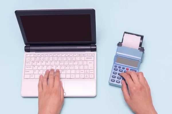 Handtippen auf einem Laptop und eine Registrierkasse auf blauem Hintergrund. Verkäufer gibt Betrag an Kasse ein — Stockfoto