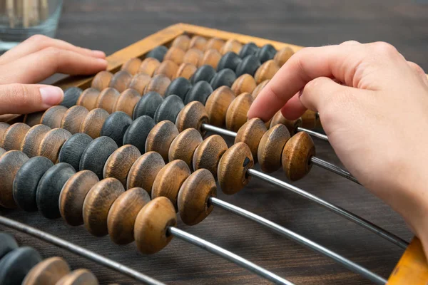 Female hand counting on ancient retro old abacus, moving beads on a wooden background, copy of space, close-up. — Stock Photo, Image