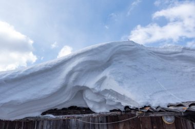 Çatıda kar yağışı bulutlu mavi gökyüzüne karşı, yakın çekim. Kar fırtınasından sonra kar yağışı.