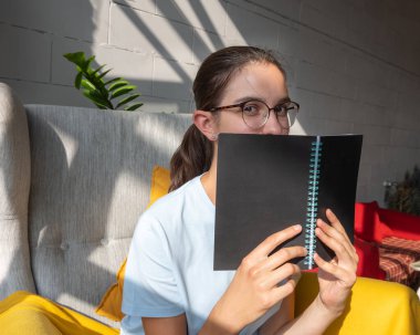 Güzel bir kız öğrenci, şık köşeli gölgeli bir kafede oturmuş kitap okuyor. Sert bir ışık. Kağıt kitap okuma kavramı. Okul konseptine geri dönelim. Serbest konsept