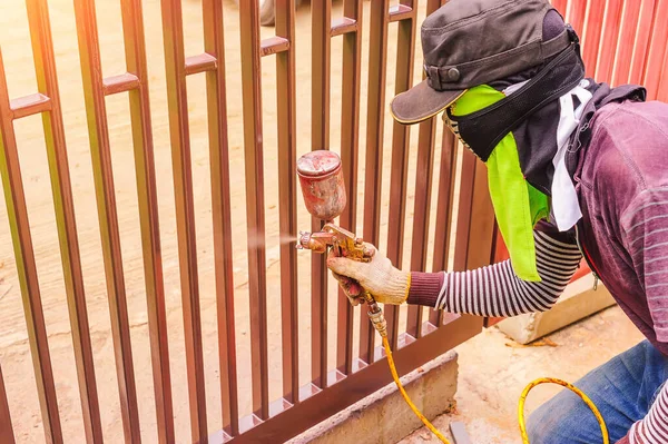 Male workers are using a paint sprayer at a steel door. Workers spray paint must be protected from inhalation by using cloth to cover the nose.