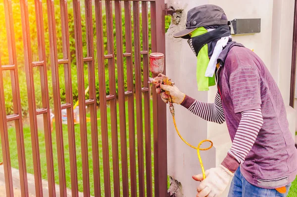 Male workers are using a paint sprayer at a steel door. Workers spray paint must be protected from inhalation by using cloth to cover the nose.