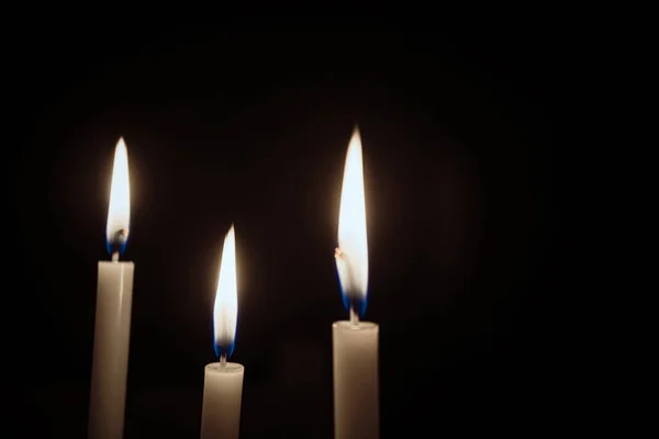 White Candles Burning in the Dark with lights glow. The burning candle's flame in the dark background. a symbol of the Christian faith. Candles Burning in the Dark with lights glow.
