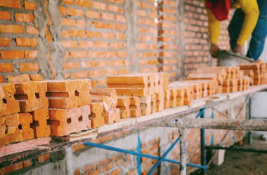 İnşaat işçilerinin çalıştığı şantiyedeki turuncu tuğlalara odaklan. Turuncu tuğlalar istiflendi ve kullanılmaya hazır. Duvarları turuncu terakotta tuğlalarıyla ayırın..