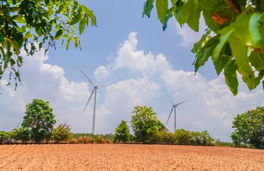 Mavi gökyüzü ve yeşil çevresi olan beyaz yel değirmeni, halkın yararı için elektrik üreten tek bir rüzgar türbini, mavi gökyüzü olan bir tarlanın ortasında duran büyük bir yel değirmeni.. 