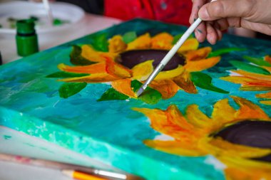Fırçalı bir el, tuval üzerinde akrilik boya kullanarak ayçiçeklerinin resmini çiziyor. Sanat konsepti.